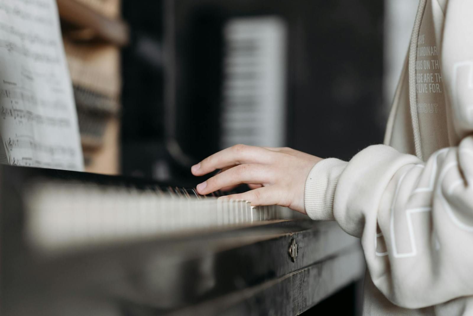 A student's hands playing an upright piano with sheet music